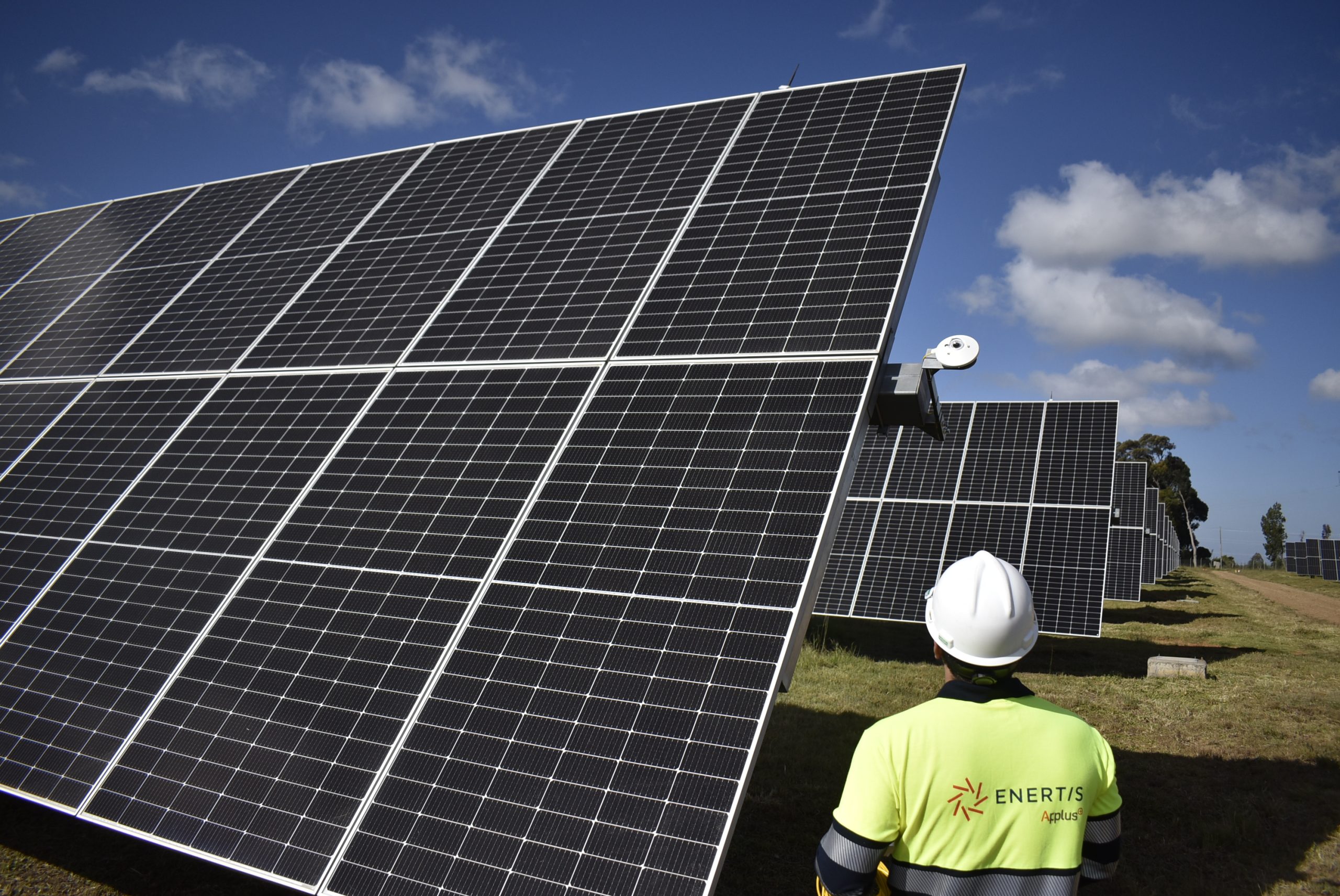 Engineer inspecting large solar panel array at a utility‑scale solar farm under a clear blue sky, highlighting renewable energy technology and solar power operations.
